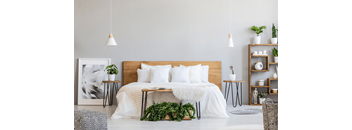 A bedroom with a bed, plants, and a picture frame on the wall.