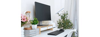 A black monitor sits on a desk with a keyboard and a plant.