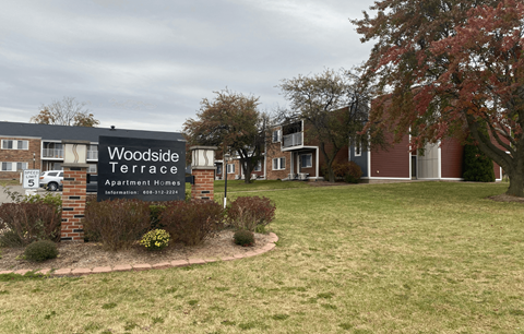 A sign for Woodside Terrace Apartment Homes is displayed in front of a grassy area.