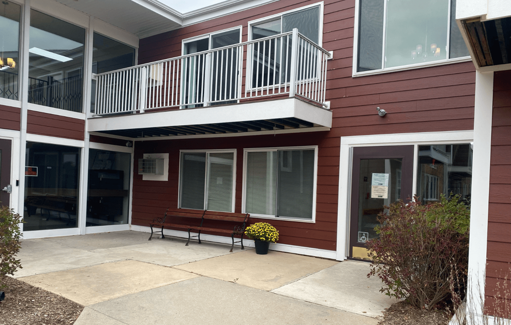 A red building with a balcony and a bench in front.