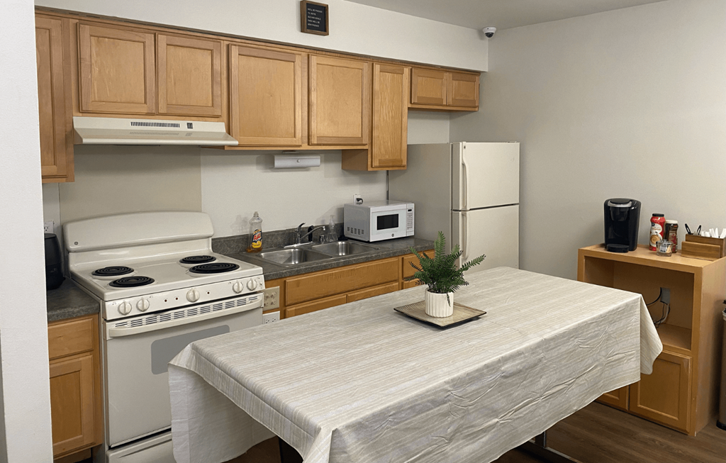A kitchen with a white stove and a white table with a plant on it.