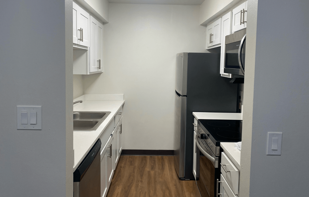 A kitchen with a black refrigerator, white cabinets, and a wooden floor.