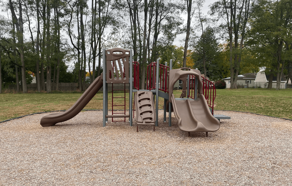 A playground with a red and grey slide and a brown slide.