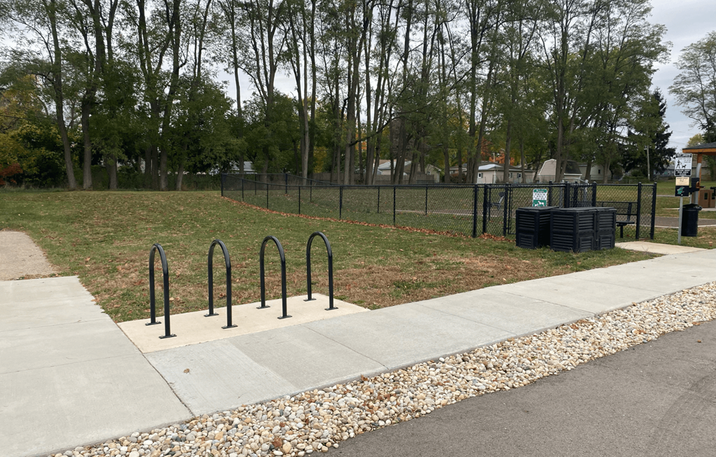 A park with a fence, trees, and a trash can.