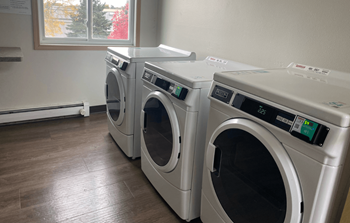 Three front load washing machines are lined up in a laundry room.
