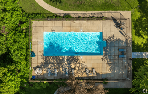 An aerial view of a rectangular swimming pool surrounded by a concrete patio and a grassy area.