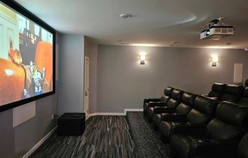 A home theater with a row of black leather chairs and a large screen.
