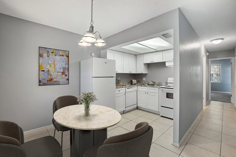 A kitchen with a table and chairs in the foreground and a refrigerator in the background.