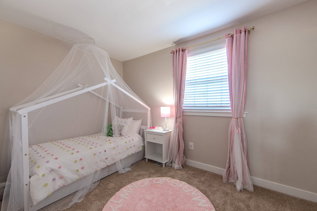 A white bed with a canopy and a pink rug in the middle of the room.