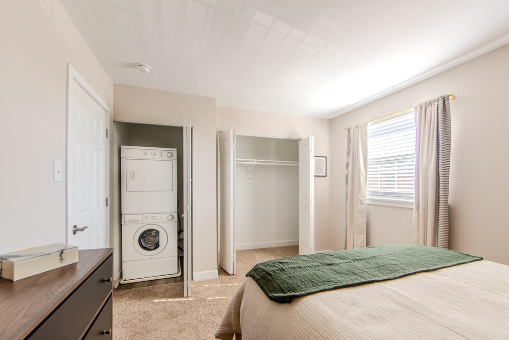 A bedroom with a bed, a washing machine, and a refrigerator in the kitchen area.