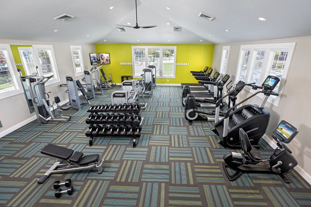 a gym with cardio equipment and weights in a room with windows