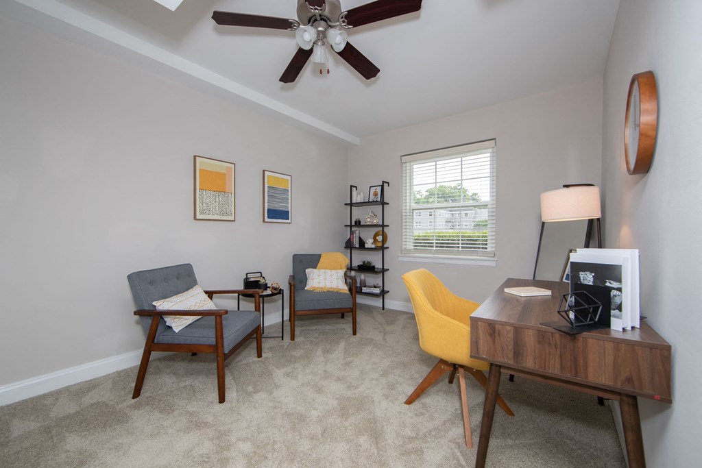 a living room with a desk and chairs and a ceiling fan