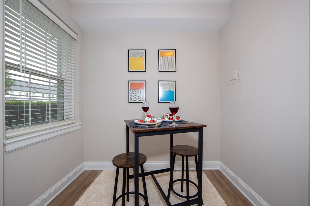 a dining room with two stools and a table with two glasses of wine