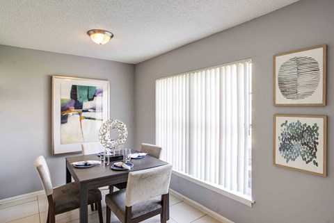 A dining room with a table set for two and a window with blinds.