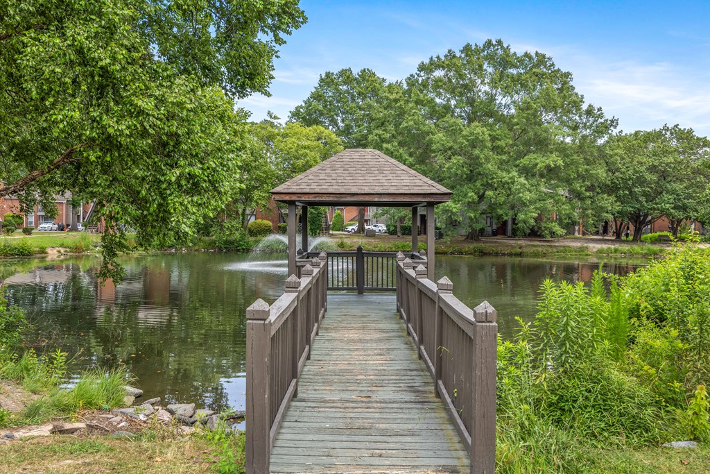 A wooden pier leads to a gazebo over a lake surrounded by trees.