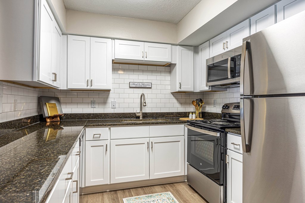 A renovated kitchen with white cabinets, stainless steel appliances and a black granite countertop.