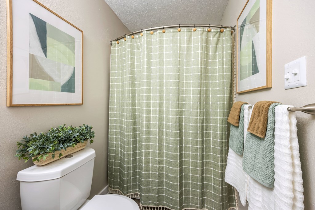 A bathroom with a green checkered shower curtain and a towel hanging on the towel rack.