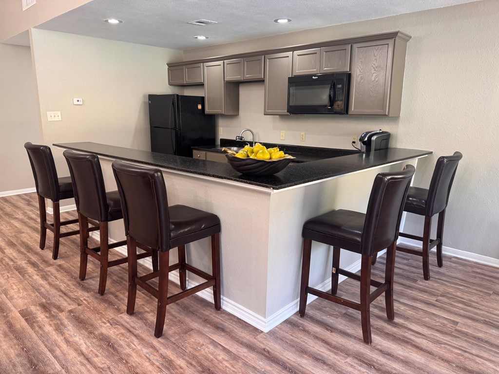 A kitchen with a black counter top and brown chairs.