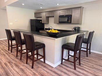 A kitchen with a black counter top and brown chairs.
