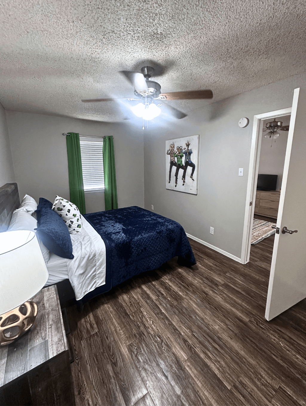 A bedroom with a bed, a ceiling fan, and a painting on the wall.