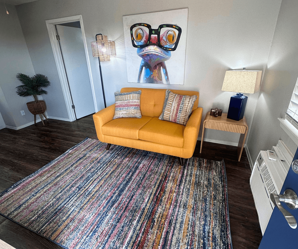 A living room with a yellow couch and a colorful rug.