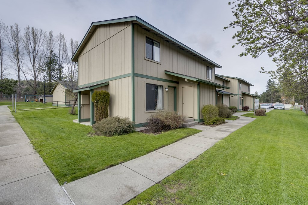 a green and tan house with a sidewalk in front of it