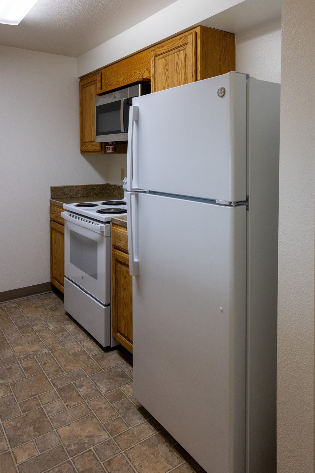 A white refrigerator stands in a kitchen with a microwave and stove.