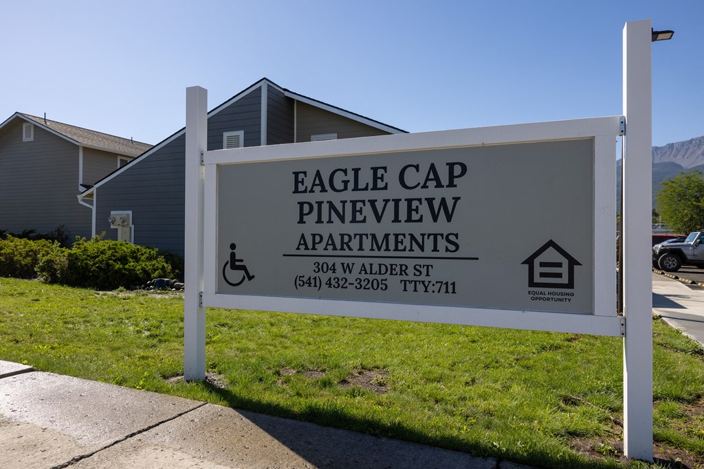 A sign for Eagle Cap Pineview Apartments is displayed in front of some houses.