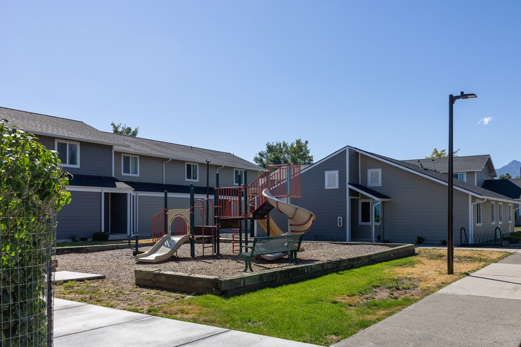 A playground with a slide and swings in front of a row of houses.