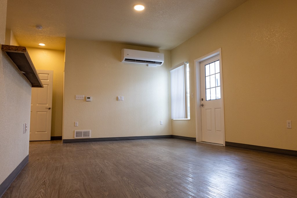 A room with a wooden floor, a window with blinds, and a door.