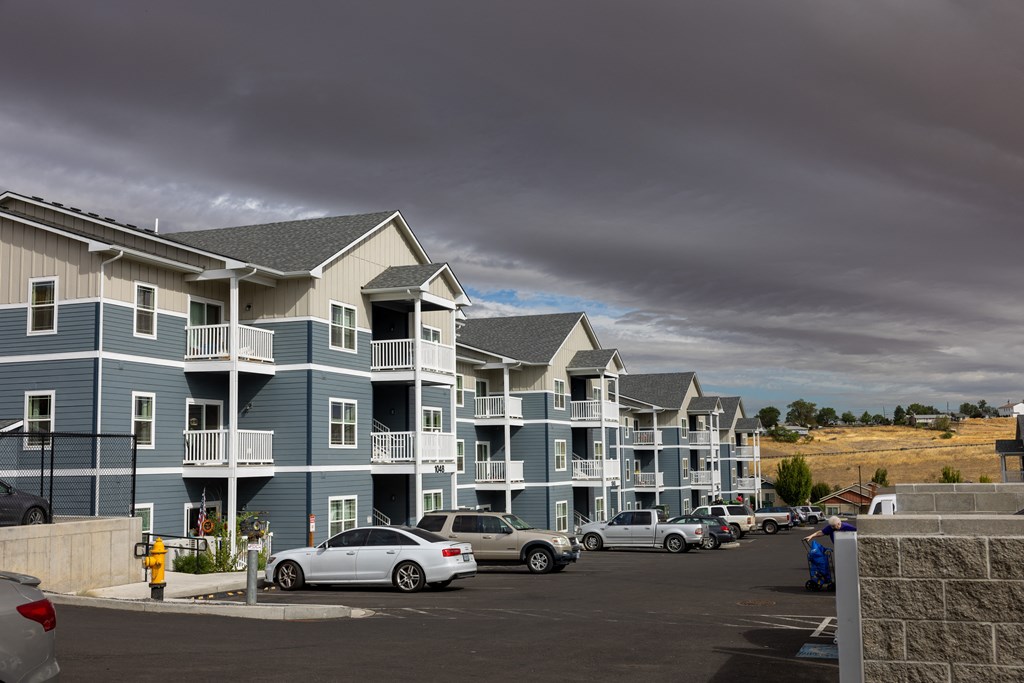 A row of apartment buildings with cars parked in front.