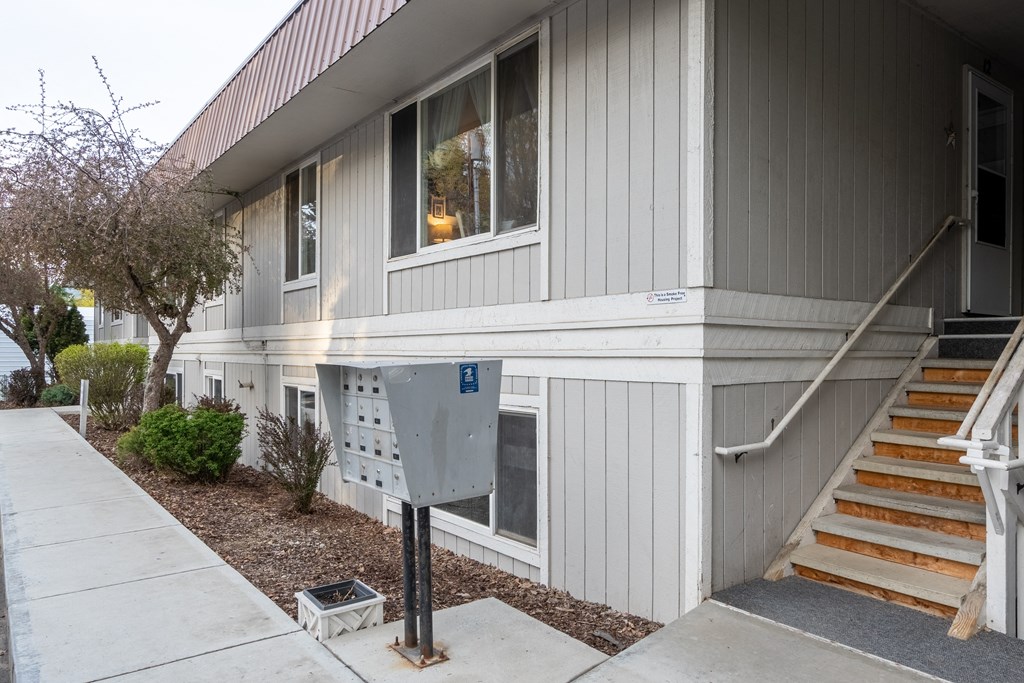 the side of a gray house with stairs and a mailbox