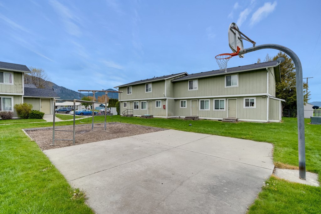 the basketball hoop is in the center of the concrete court in front of a house