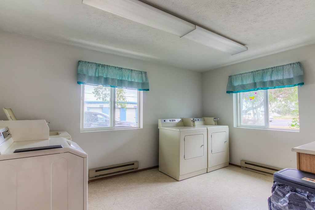 A room with two windows, a white cabinet, and a white dresser.