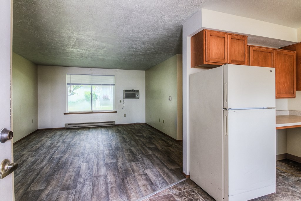 A room with a white fridge and wooden floors.
