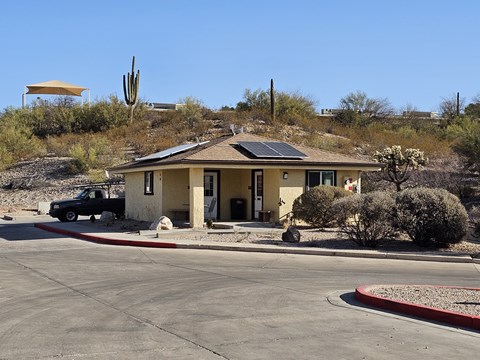 A house with a solar panel on the roof is surrounded by a desert landscape.