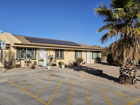 A building with solar panels on the roof and a parking lot in front.