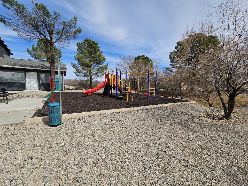A playground with a slide, swings, and a blue trash can.