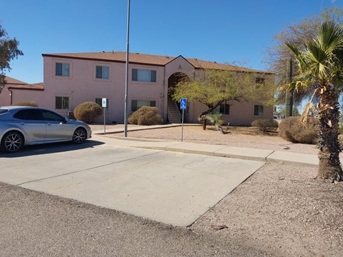 A silver car is parked in front of a pink building with a blue handicap sign.