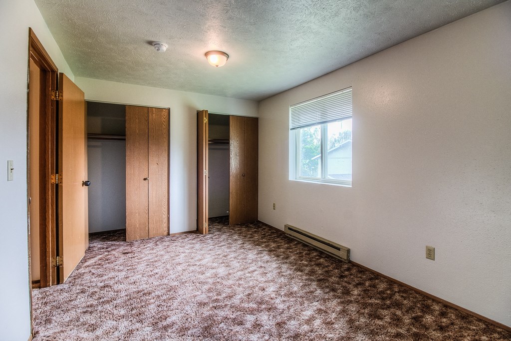 A room with a carpeted floor and a window with blinds.