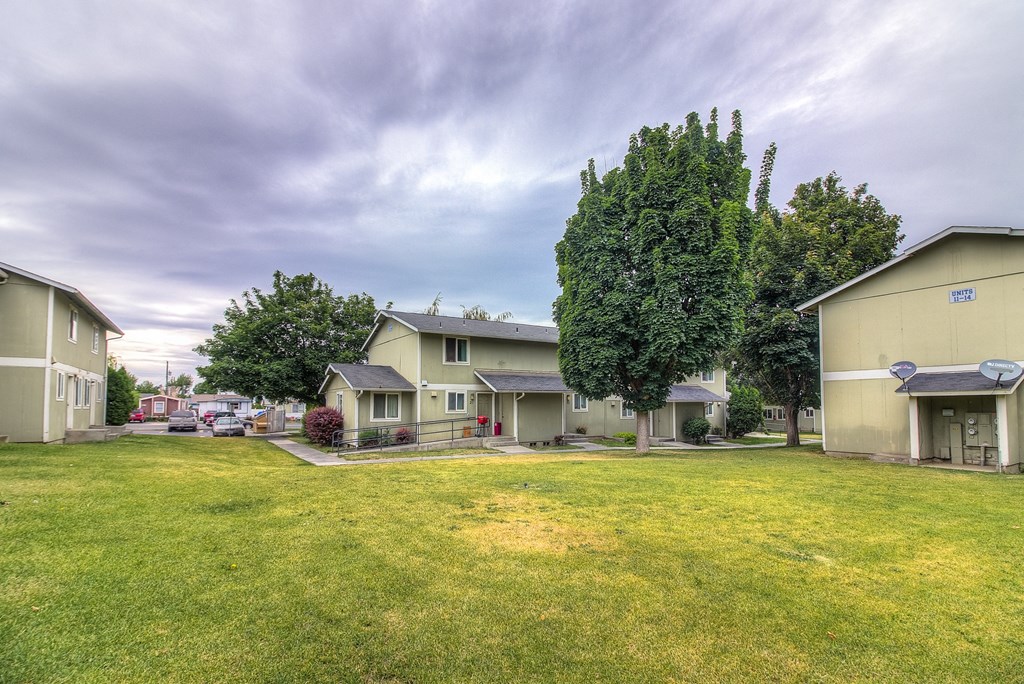A grassy field with a few houses and trees in the background.