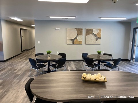 A conference room with a round table and chairs, a vase with flowers, and two abstract paintings on the wall.
