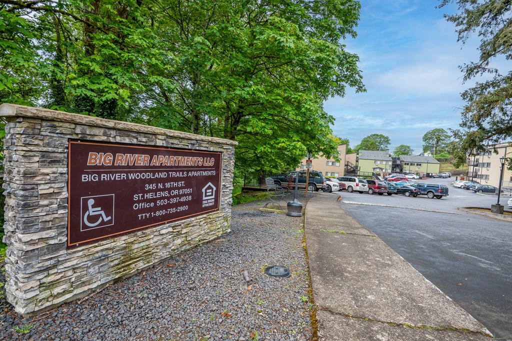 A sign for Big River Apartments stands in front of a parking lot.