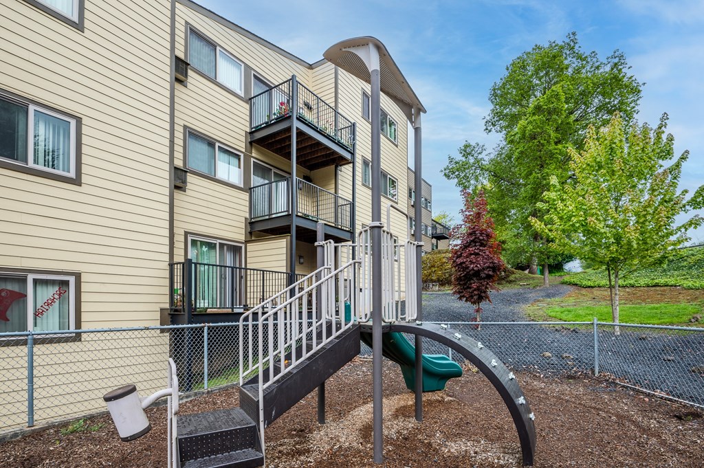A playground with a slide is in front of a building.