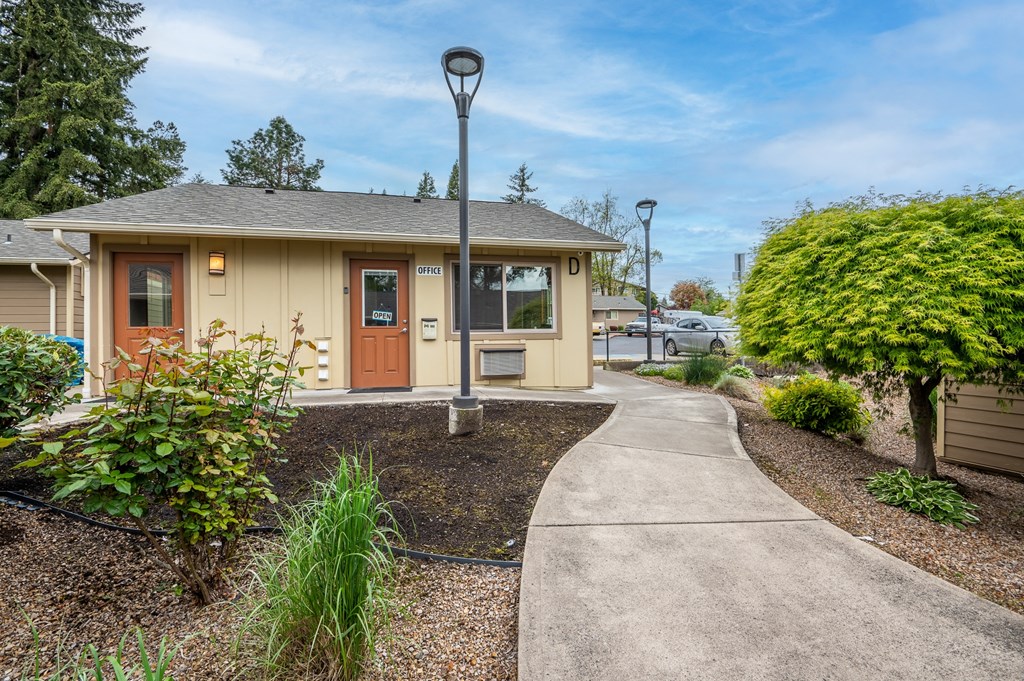 A small building with a brown door is surrounded by a gravel area and a concrete walkway.