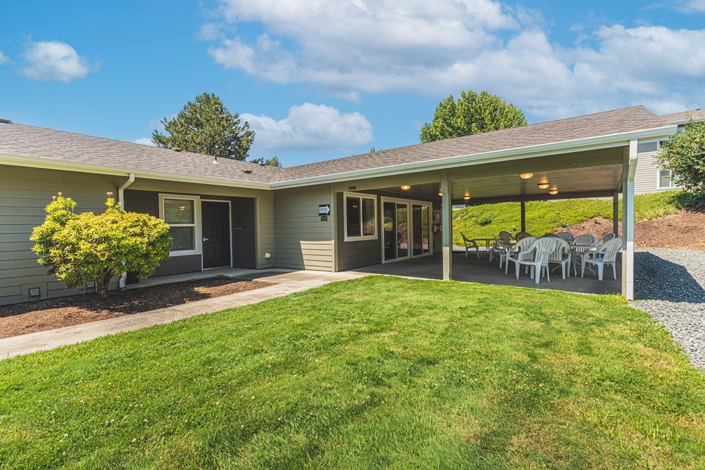 a backyard with a lawn and a patio with tables and chairs