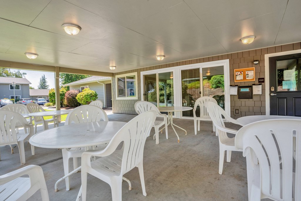 a patio with white chairs and tables and windows