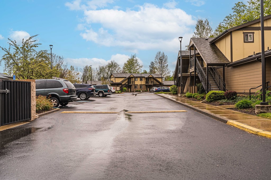 a wet street with houses and cars parked in a parking lot