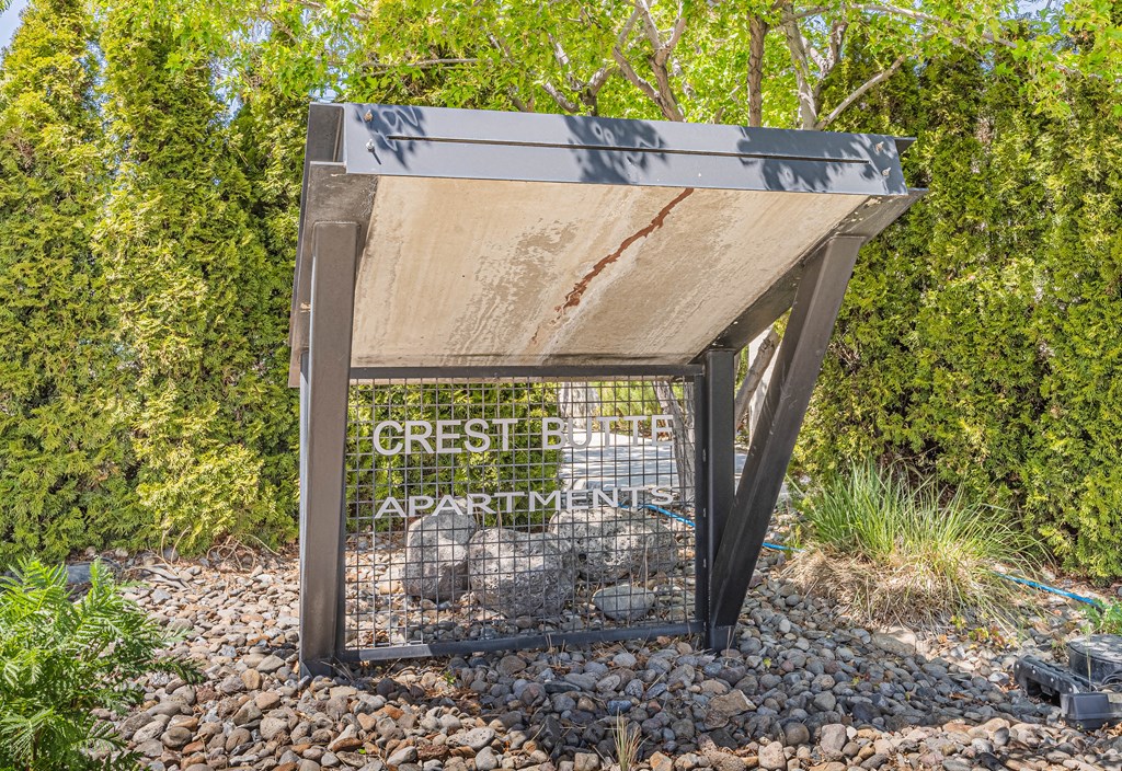 A sign for Crest Apartments is displayed in front of a green hedge.