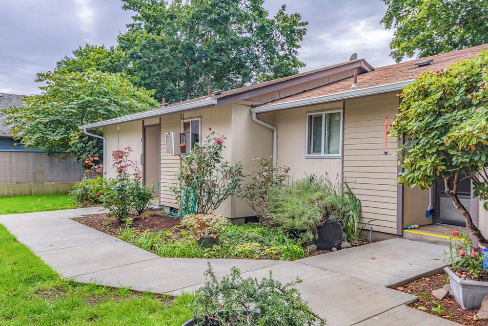 a small tan house with a sidewalk in front of it